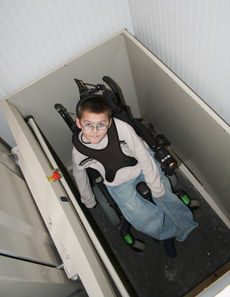 Boy in a wheelchair in an in-home elevator looking up at the camera